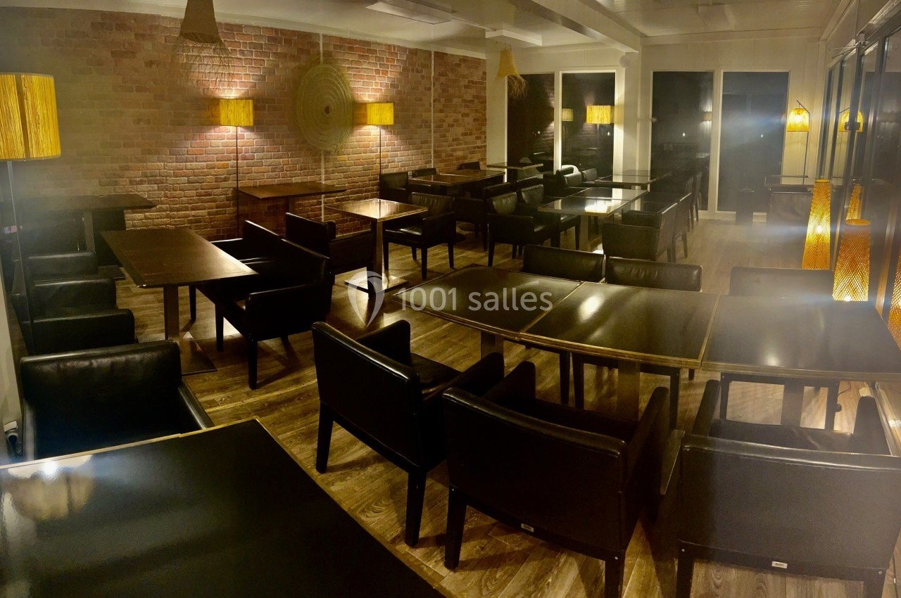 Salle de restaurant vide avec mobilier en bois et cuir, éclairée par des lampes chaleureuses et un mur en briques apparentes.