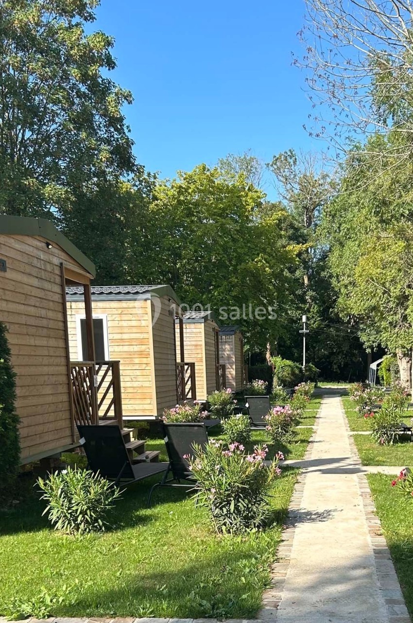 Allée bordée de mobil-homes en bois entourés de verdure sous un ciel bleu clair.