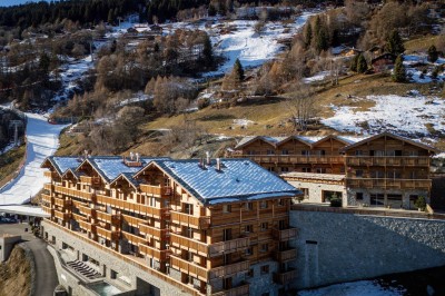 Vue aérienne d'un village de montagne enneigé entouré de sommets alpins sous un ciel dégagé.