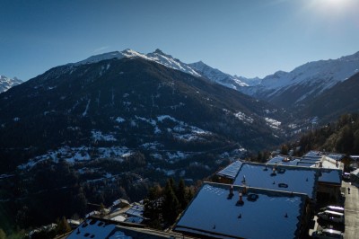 Vue aérienne d'un village de montagne enneigé entouré de sommets alpins sous un ciel dégagé.