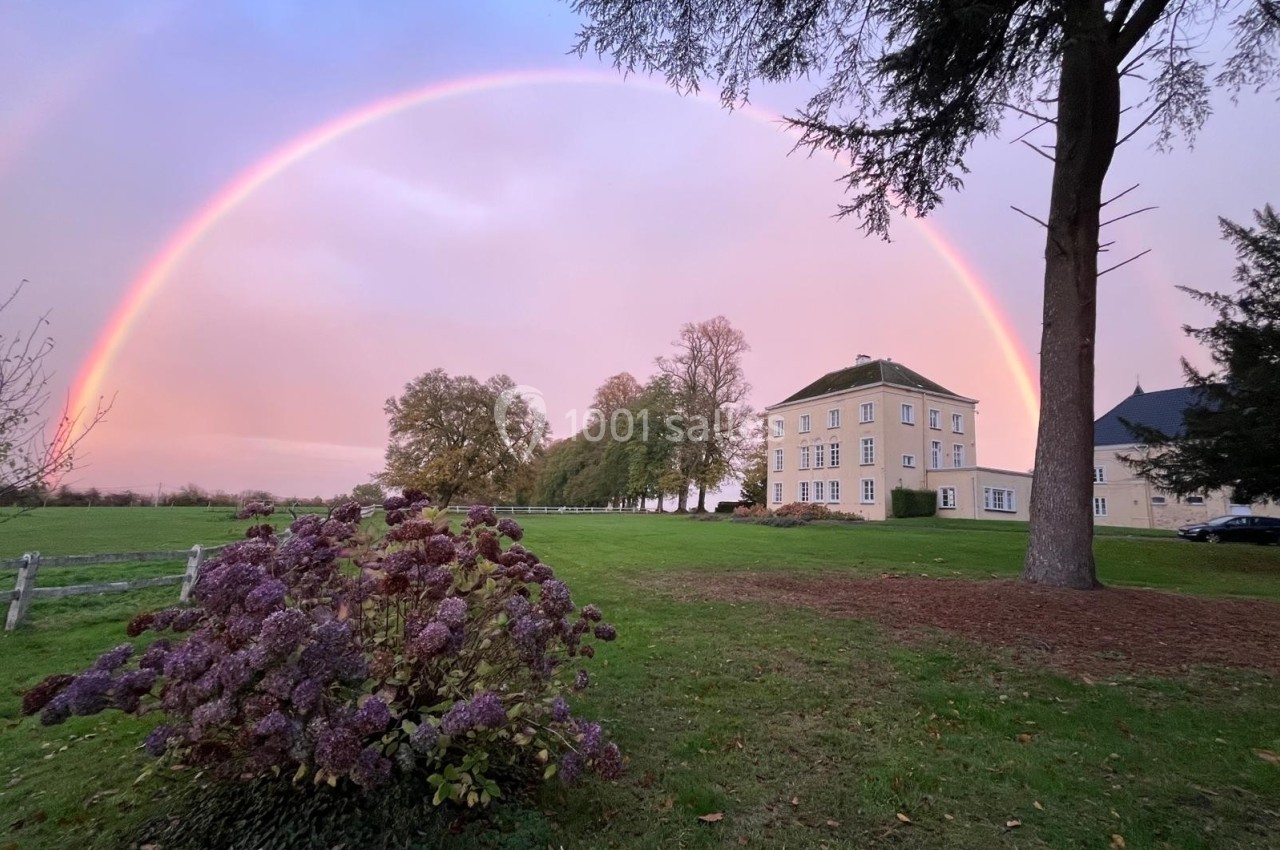 Un arc-en-ciel au-dessus d'un grand bâtiment entouré d'arbres et d'un jardin avec des hortensias.
