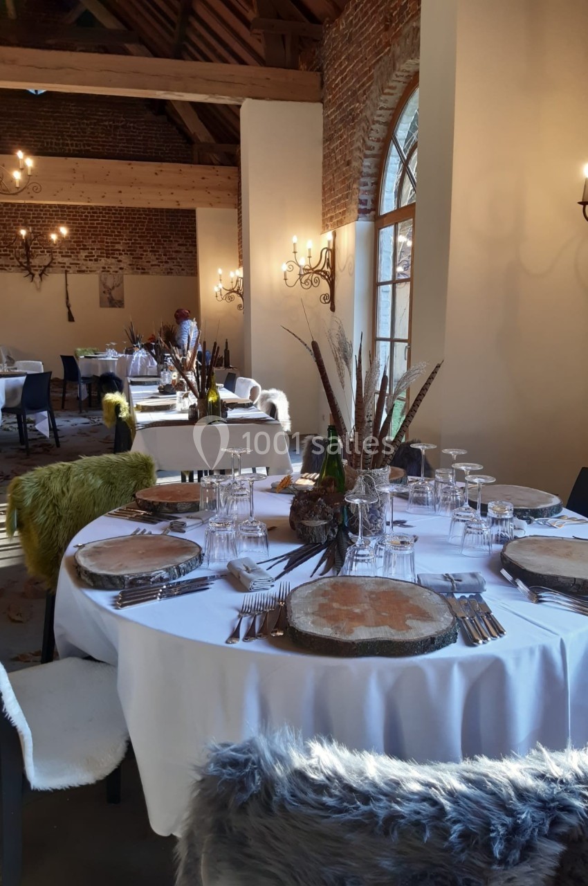 Salle de réception décorée avec des tables rondes dressées, ornées de centres de table naturels et éclairée par des lustres.