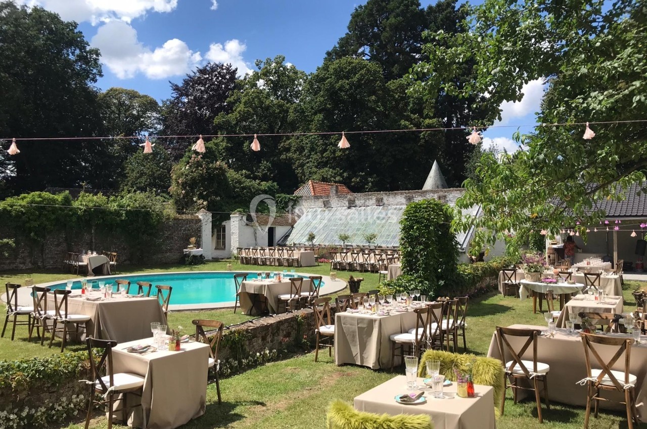 Tables dressées pour un événement en plein air autour d'une piscine, dans un jardin entouré de verdure.