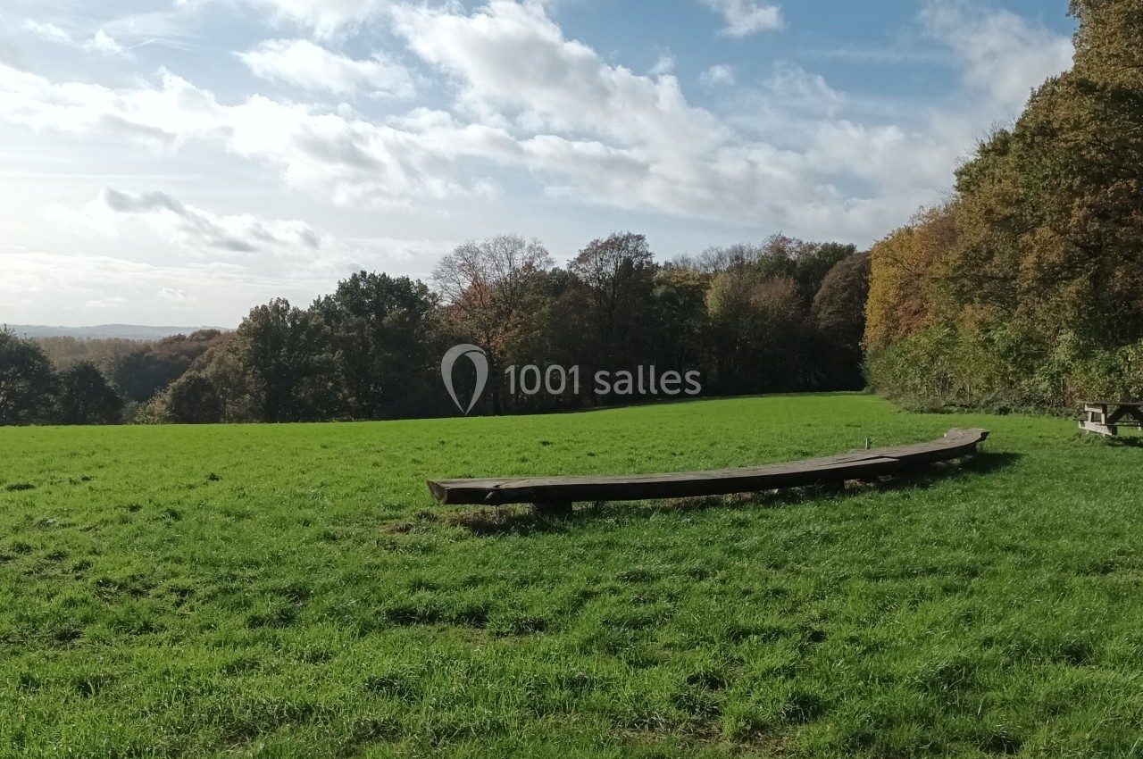 Une prairie verdoyante avec un banc en bois au premier plan, bordée par une forêt sous un ciel partiellement nuageux.