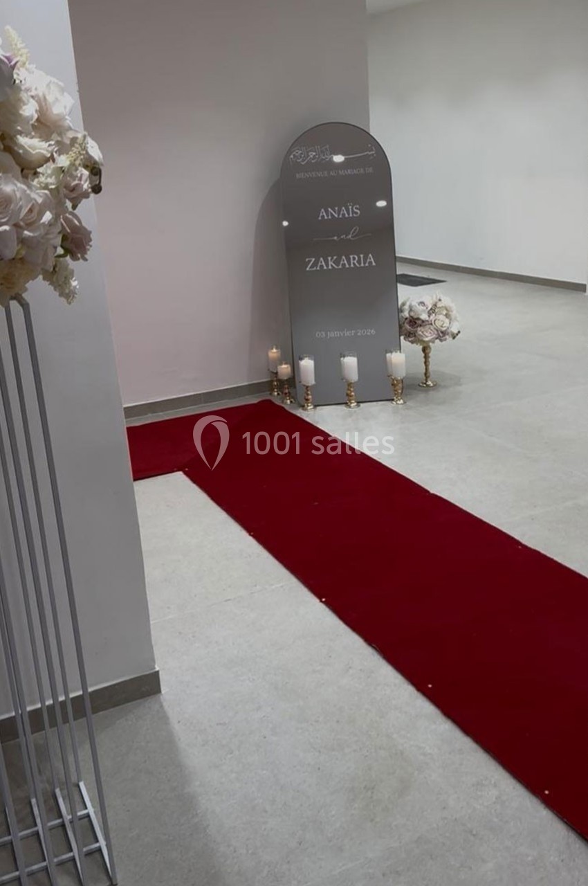 Tapis rouge menant à un panneau décoratif avec des bougies et des fleurs dans une salle sobre.