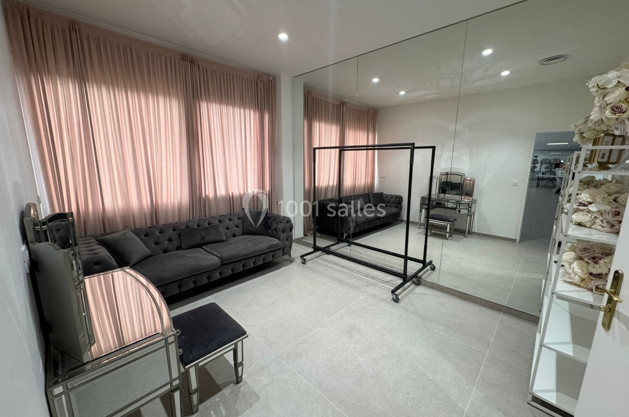 Salle lumineuse avec canapé gris, miroir mural, rideaux roses, étagères décorées et mobilier moderne.