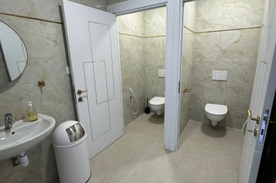 Salle de bain avec lavabo, miroir, poubelle et deux toilettes séparées par des cloisons.
