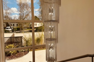 Lustre en cristal suspendu dans une cage d'escalier lumineuse avec vue sur un jardin et des bâtiments à travers une grande…