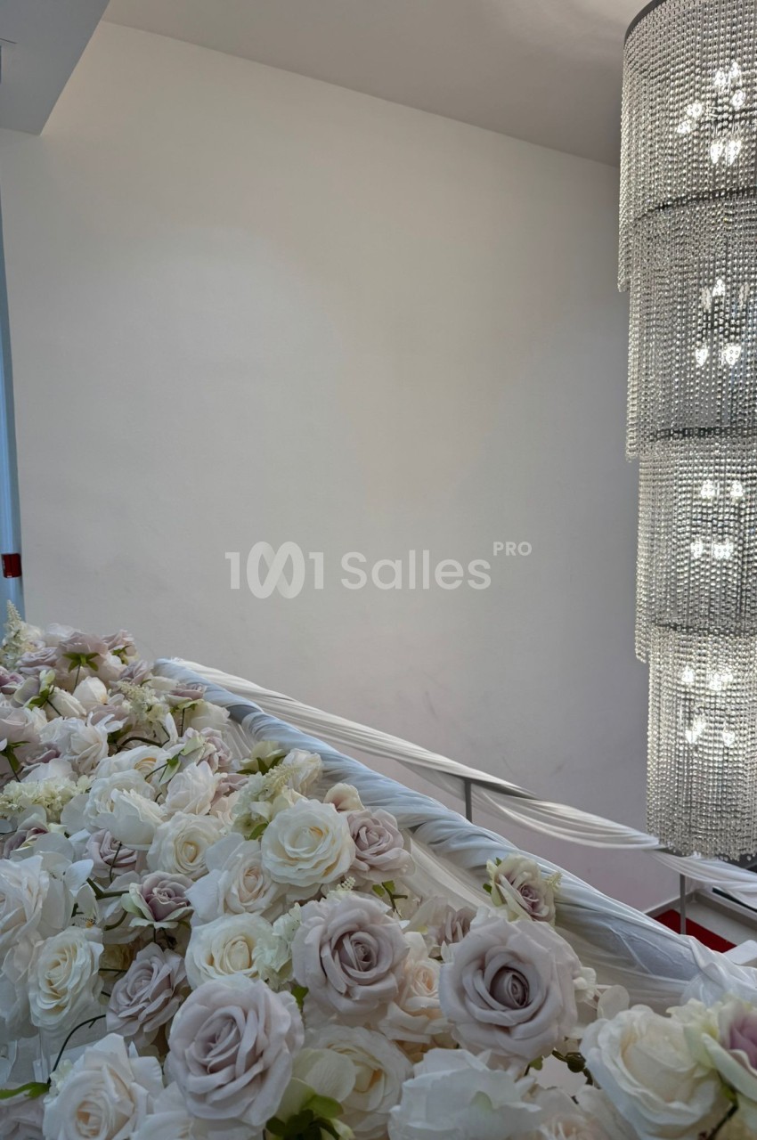 Décoration florale blanche et pastel sur une rambarde, avec un lustre en cristal suspendu dans un espace lumineux.