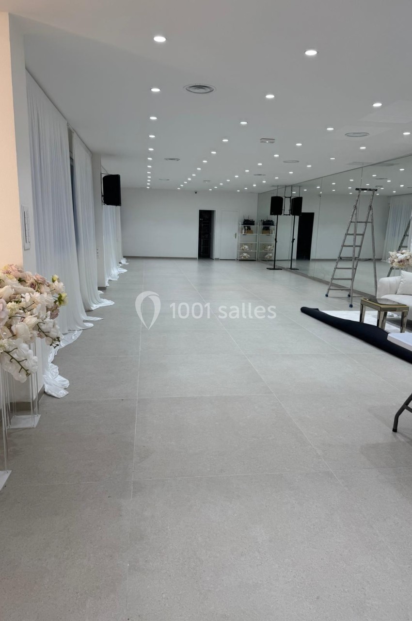 Salle lumineuse avec sol en carrelage clair, décor floral, rideaux blancs, échelle et mobilier en cours d'installation.