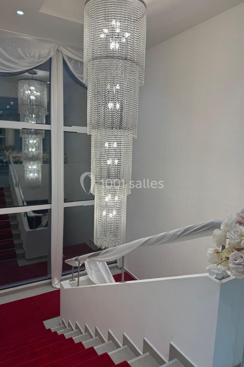 Escalier recouvert de tapis rouge avec un lustre en cristal suspendu et des décorations florales blanches.