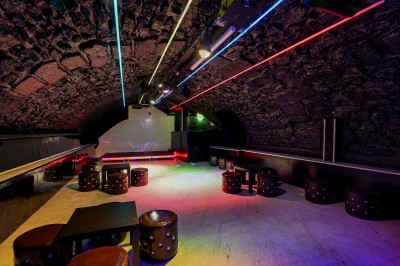 Salle sombre aux murs en pierre noire, équipée de tables hautes blanches et d'un sol en carrelage gris.