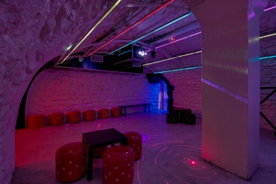 Salle sombre aux murs en pierre noire, équipée de tables hautes blanches et d'un sol en carrelage gris.