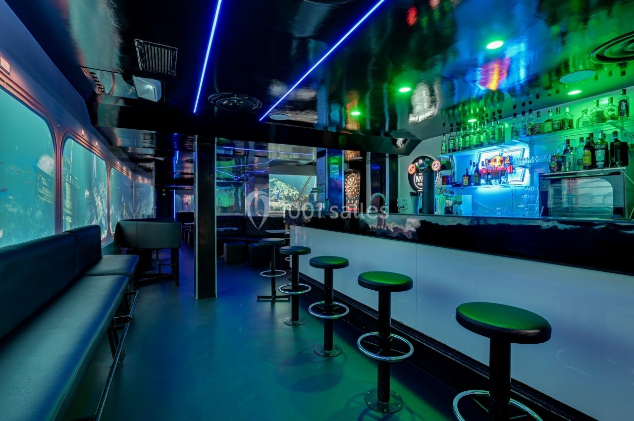 Intérieur d'un bar moderne avec éclairage néon bleu et vert, comptoir blanc et tabourets alignés.