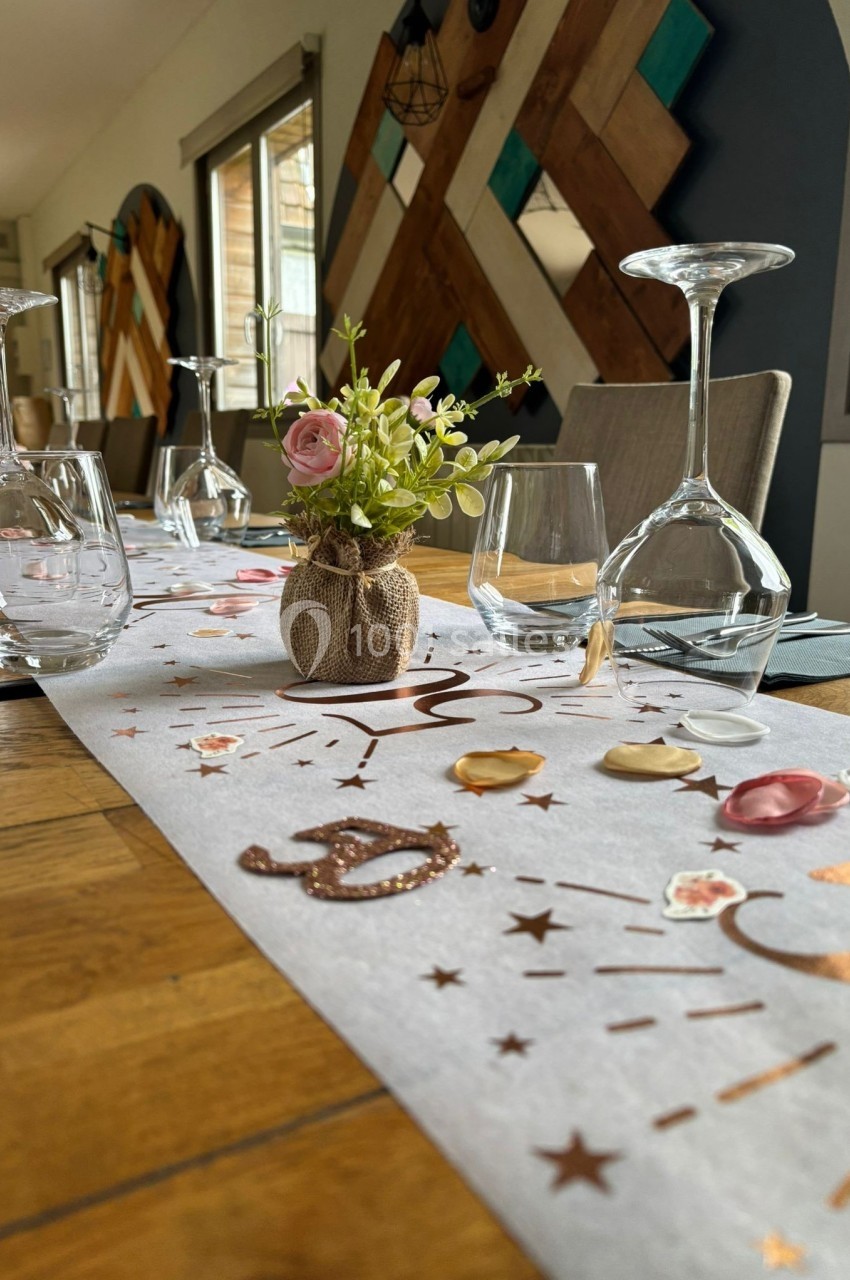 Chemin de table décoré avec des motifs dorés, pétales et un petit vase fleuri, entouré de verres et couverts.