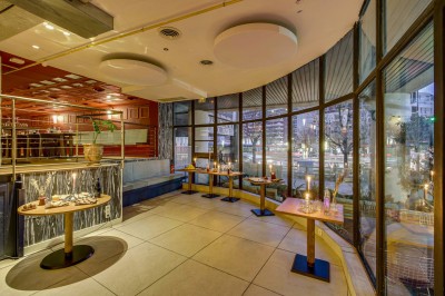 Terrasse d'un restaurant avec tables dressées, éclairage chaleureux et pergola en bois, entourée de végétation.
