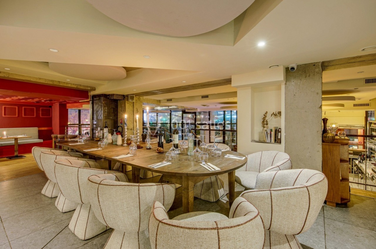 Salle de restaurant moderne avec une grande table en bois entourée de chaises design et une vue sur l'étage inférieur.