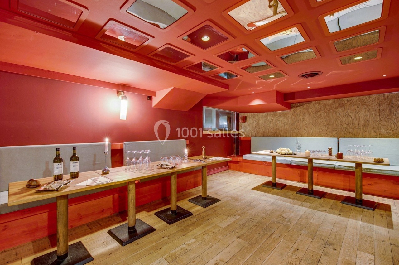 Salle de restaurant avec tables en bois dressées, murs rouges et plafond décoré de cadres réfléchissants.