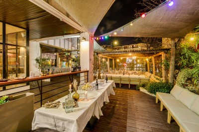 Terrasse d'un restaurant avec tables dressées, éclairage chaleureux et pergola en bois, entourée de végétation.