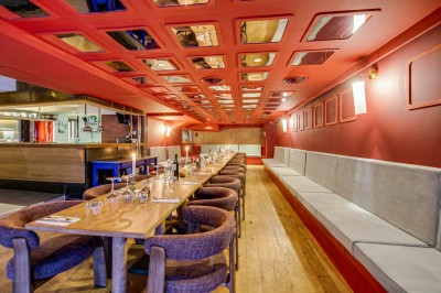 Terrasse d'un restaurant avec tables dressées, éclairage chaleureux et pergola en bois, entourée de végétation.