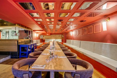 Terrasse d'un restaurant avec tables dressées, éclairage chaleureux et pergola en bois, entourée de végétation.