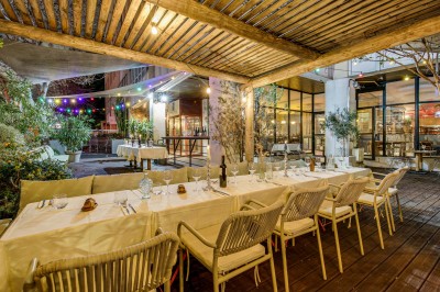 Terrasse d'un restaurant avec tables dressées, éclairage chaleureux et pergola en bois, entourée de végétation.