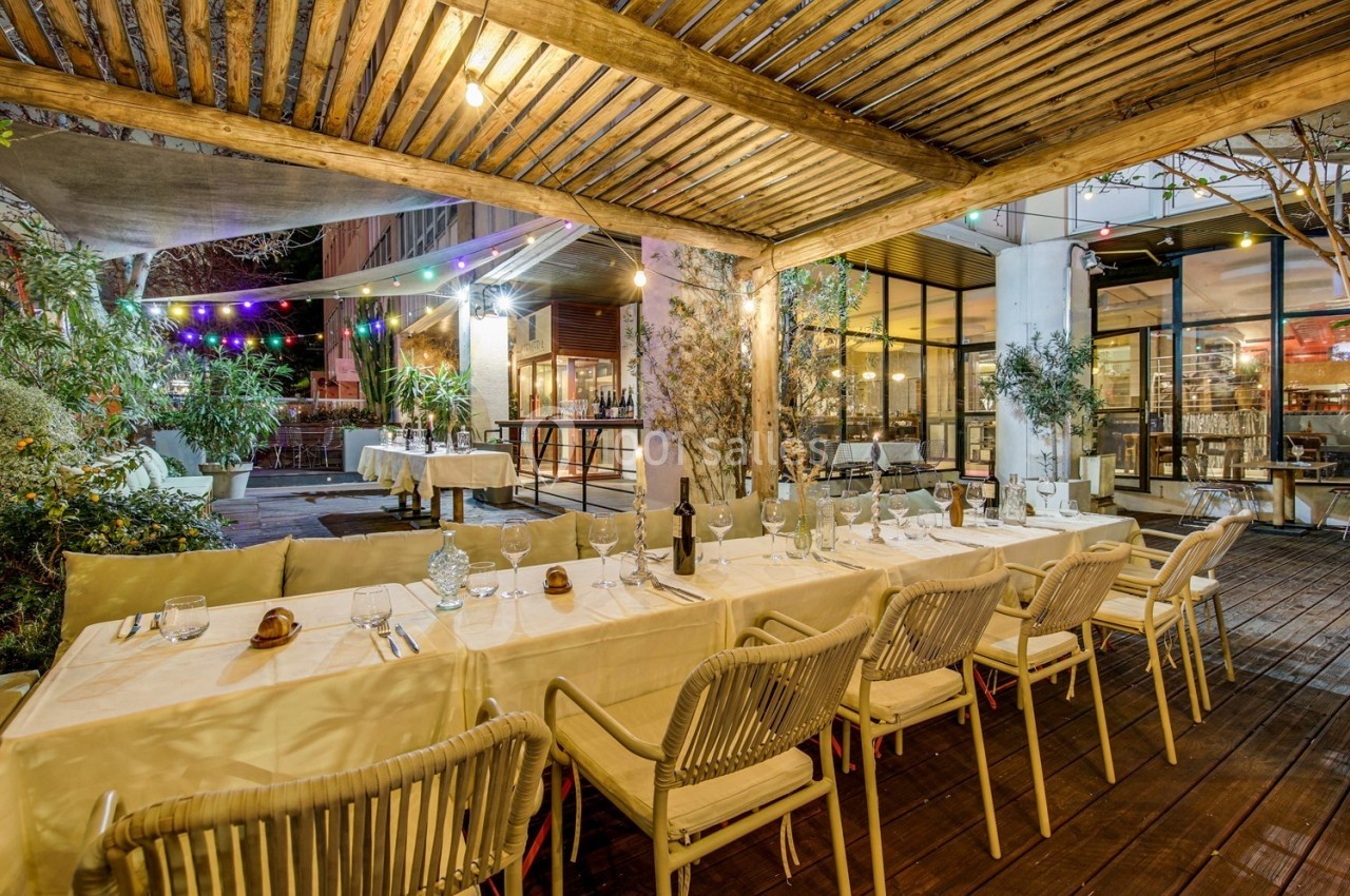 Terrasse d'un restaurant avec tables dressées, éclairage chaleureux et pergola en bois, entourée de végétation.