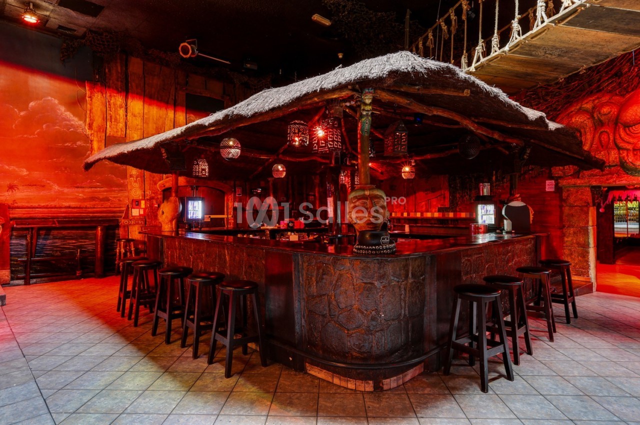 Bar à thème exotique avec toit en chaume, tabourets en bois et décorations tropicales dans une ambiance chaleureuse.
