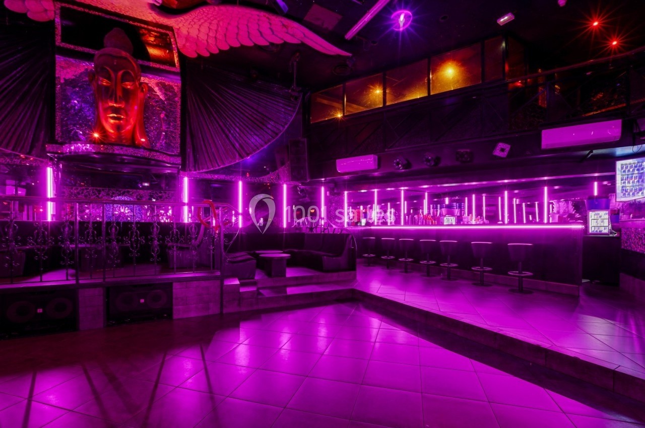 Intérieur d'une discothèque avec éclairage violet, bar avec tabourets alignés et décoration murale artistique.