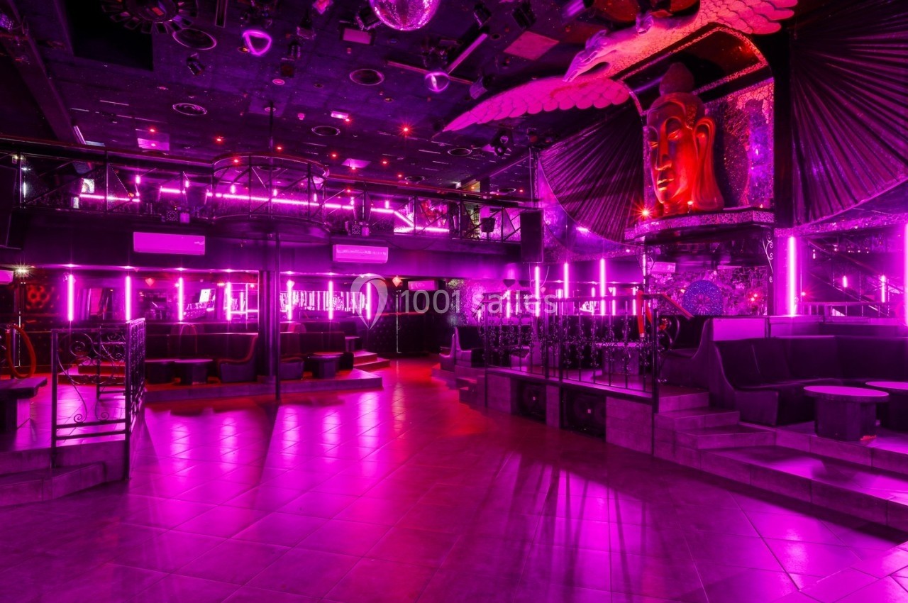 Salle de discothèque vide avec éclairage néon rose, décorations exotiques et sièges disposés autour de la piste.