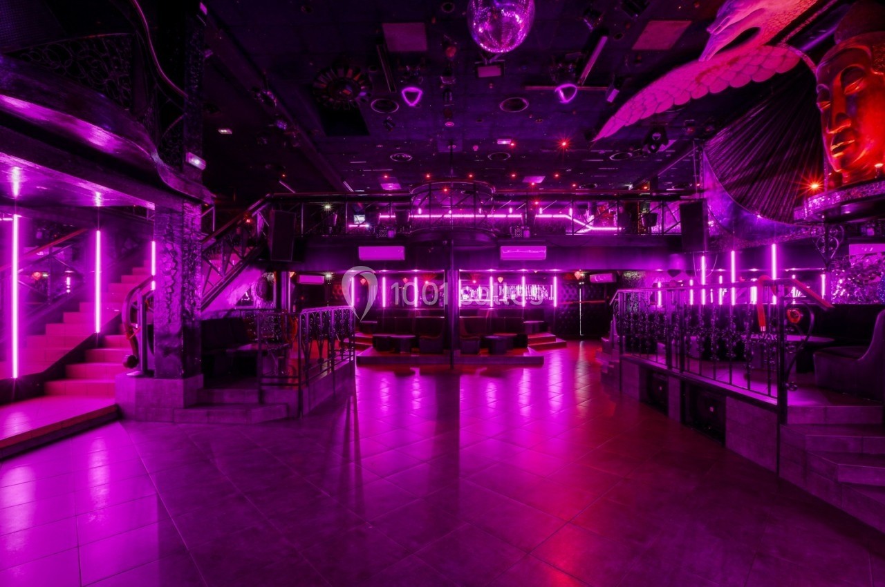 Salle de discothèque vide avec éclairage néon rose, piste de danse centrale et décorations artistiques.