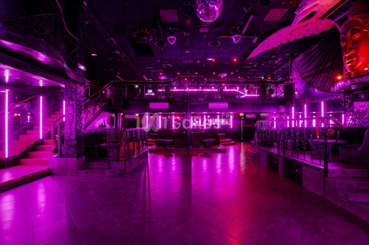 Salle de discothèque vide avec éclairage néon rose, piste de danse centrale et décorations artistiques.
