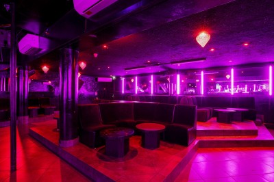 Intérieur d'une discothèque avec éclairage violet, escalier central, balustrades métalliques et sol carrelé coloré.