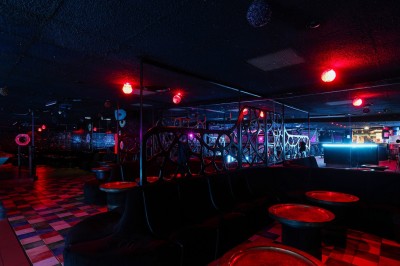 Intérieur d'une discothèque avec éclairage violet, escalier central, balustrades métalliques et sol carrelé coloré.