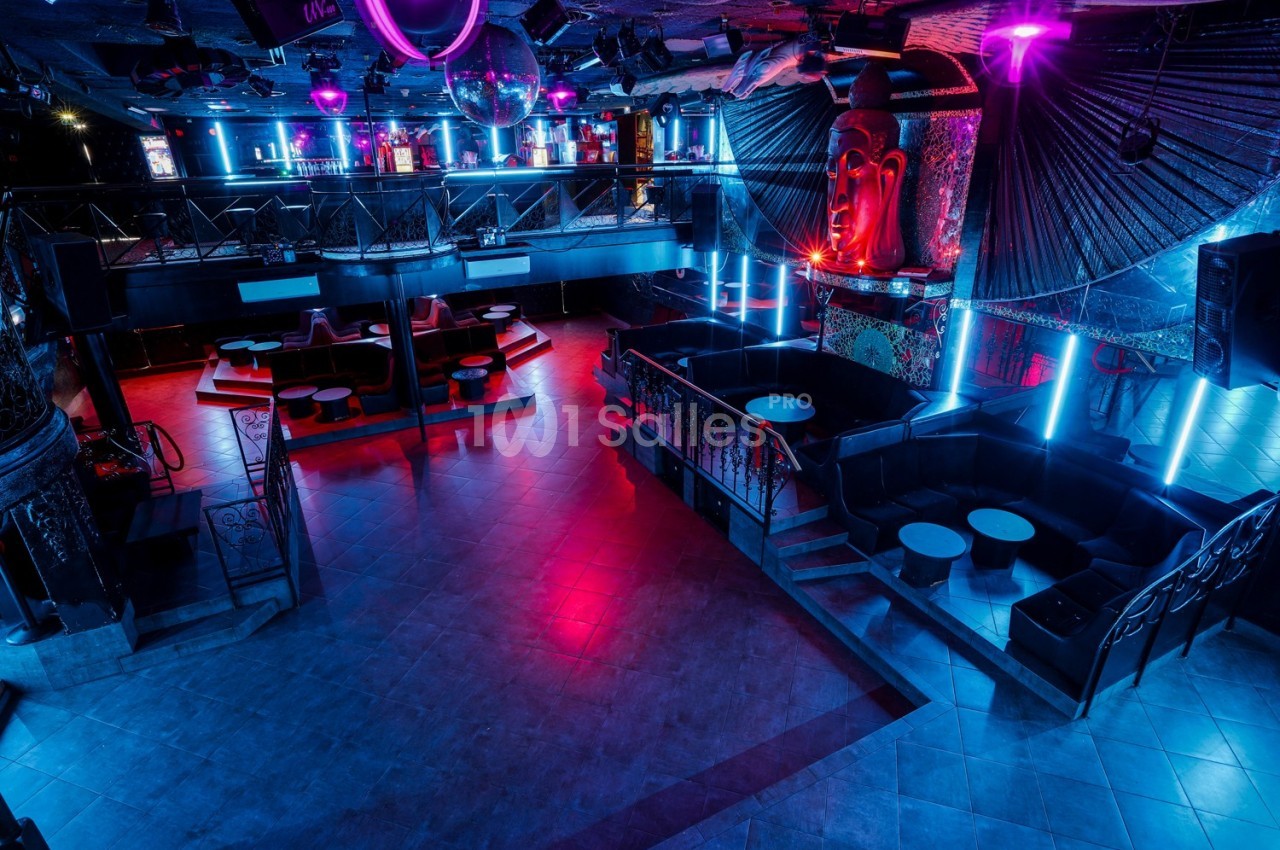 Salle de discothèque vide avec éclairage néon coloré, tables et banquettes disposées autour d'une piste de danse.