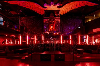 Intérieur d'une discothèque avec éclairage violet, escalier central, balustrades métalliques et sol carrelé coloré.