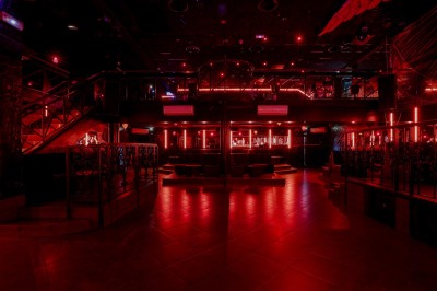 Intérieur d'une discothèque avec éclairage violet, escalier central, balustrades métalliques et sol carrelé coloré.