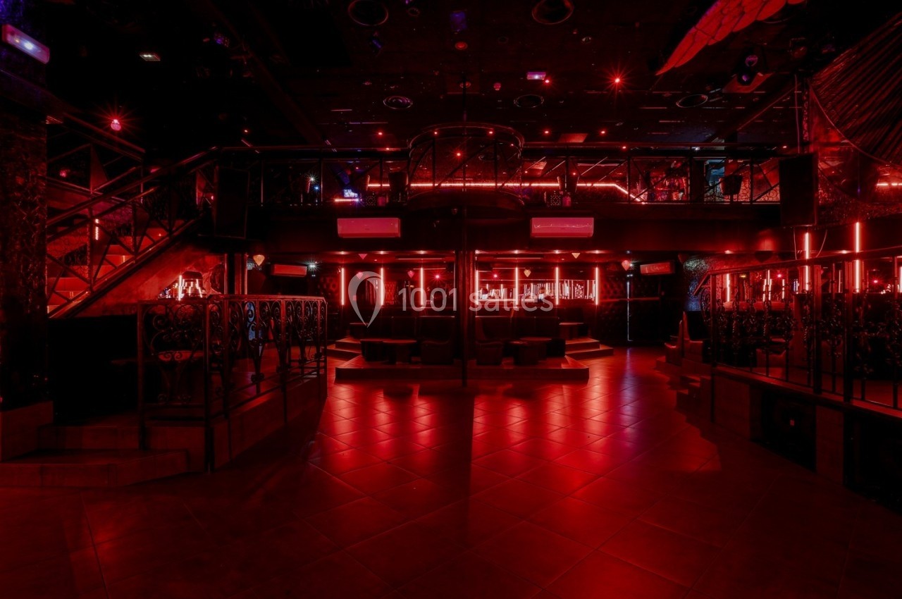 Intérieur d'une discothèque avec éclairage rouge, bar central, mezzanine et escaliers métalliques.