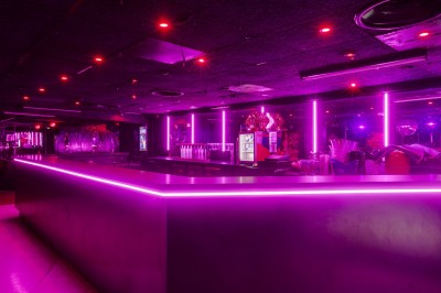 Intérieur d'une discothèque avec éclairage violet, escalier central, balustrades métalliques et sol carrelé coloré.