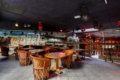 Intérieur d'une discothèque avec éclairage violet, escalier central, balustrades métalliques et sol carrelé coloré.