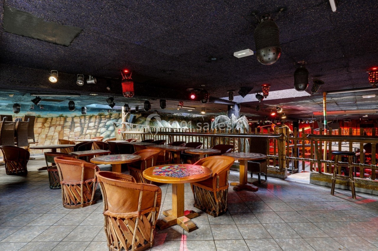 Salle de restaurant avec tables en bois, chaises en cuir et décoration intérieure évoquant un style tropical.