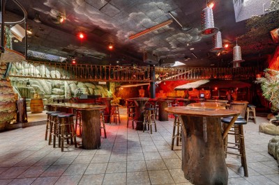 Intérieur d'une discothèque avec éclairage violet, escalier central, balustrades métalliques et sol carrelé coloré.