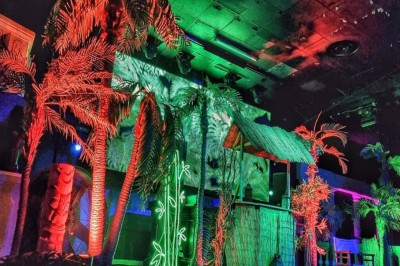 Intérieur d'une discothèque avec éclairage violet, escalier central, balustrades métalliques et sol carrelé coloré.
