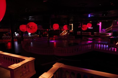 Intérieur d'une discothèque avec éclairage violet, escalier central, balustrades métalliques et sol carrelé coloré.