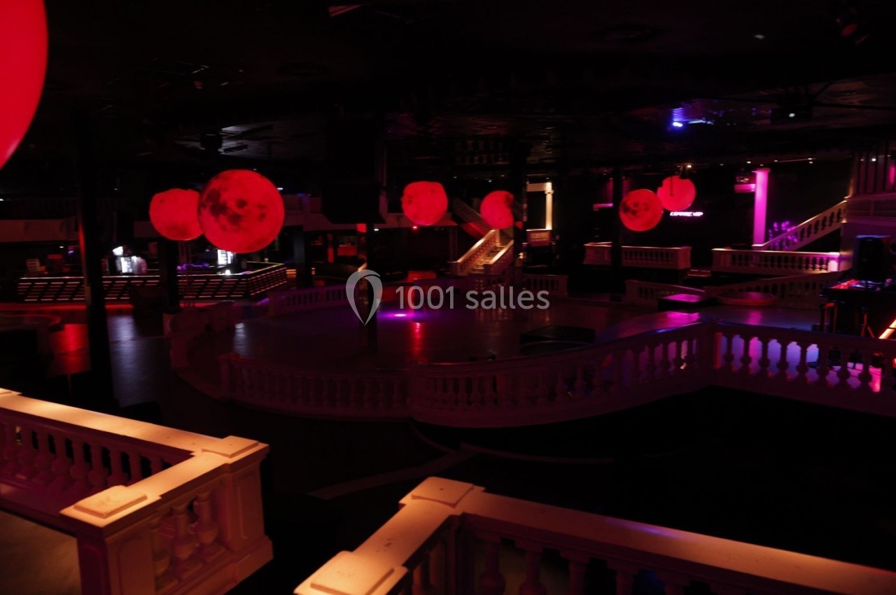 Salle de discothèque sombre avec éclairage rouge, piste de danse centrale et balustrades blanches.