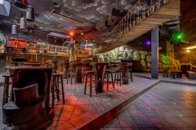 Intérieur d'une discothèque avec éclairage violet, escalier central, balustrades métalliques et sol carrelé coloré.