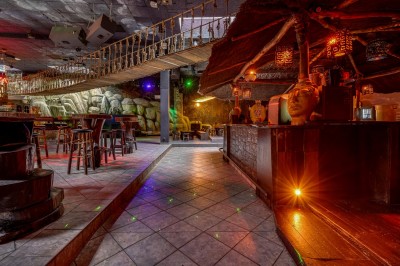 Intérieur d'une discothèque avec éclairage violet, escalier central, balustrades métalliques et sol carrelé coloré.