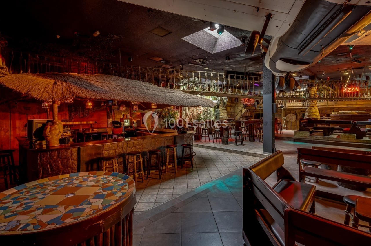 Intérieur d'un bar à thème tropical avec toit en chaume, tables en bois et éclairage tamisé.