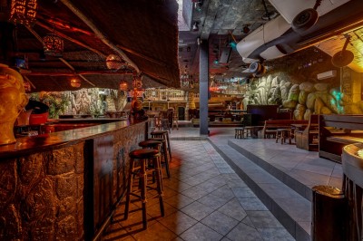 Intérieur d'une discothèque avec éclairage violet, escalier central, balustrades métalliques et sol carrelé coloré.