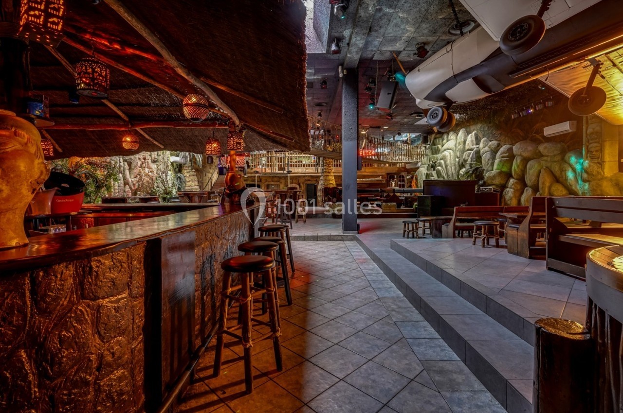 Intérieur d'un bar à thème avec comptoir en bois, tabourets, éclairage tamisé et décorations exotiques.